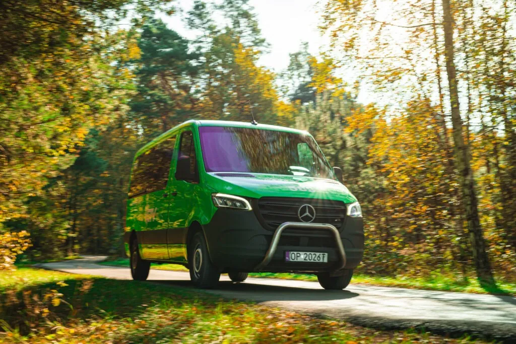 Jadący zielony bus na tle jesieni